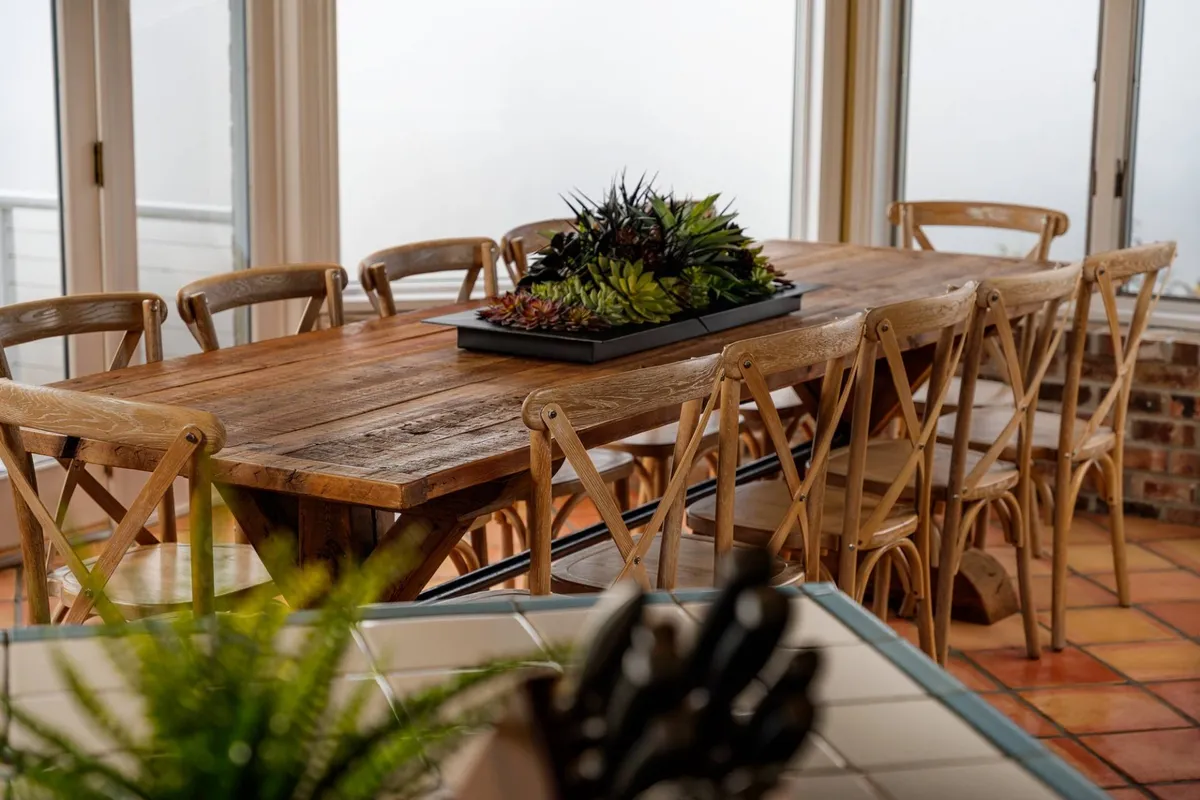 A large wooden dining table surrounded by chairs and topped with a succulent centerpiece is the focal point, creating an inviting scene for family-style dinners, celebrations, or lingering over local flavors. The overall mood is cozy and communal.
