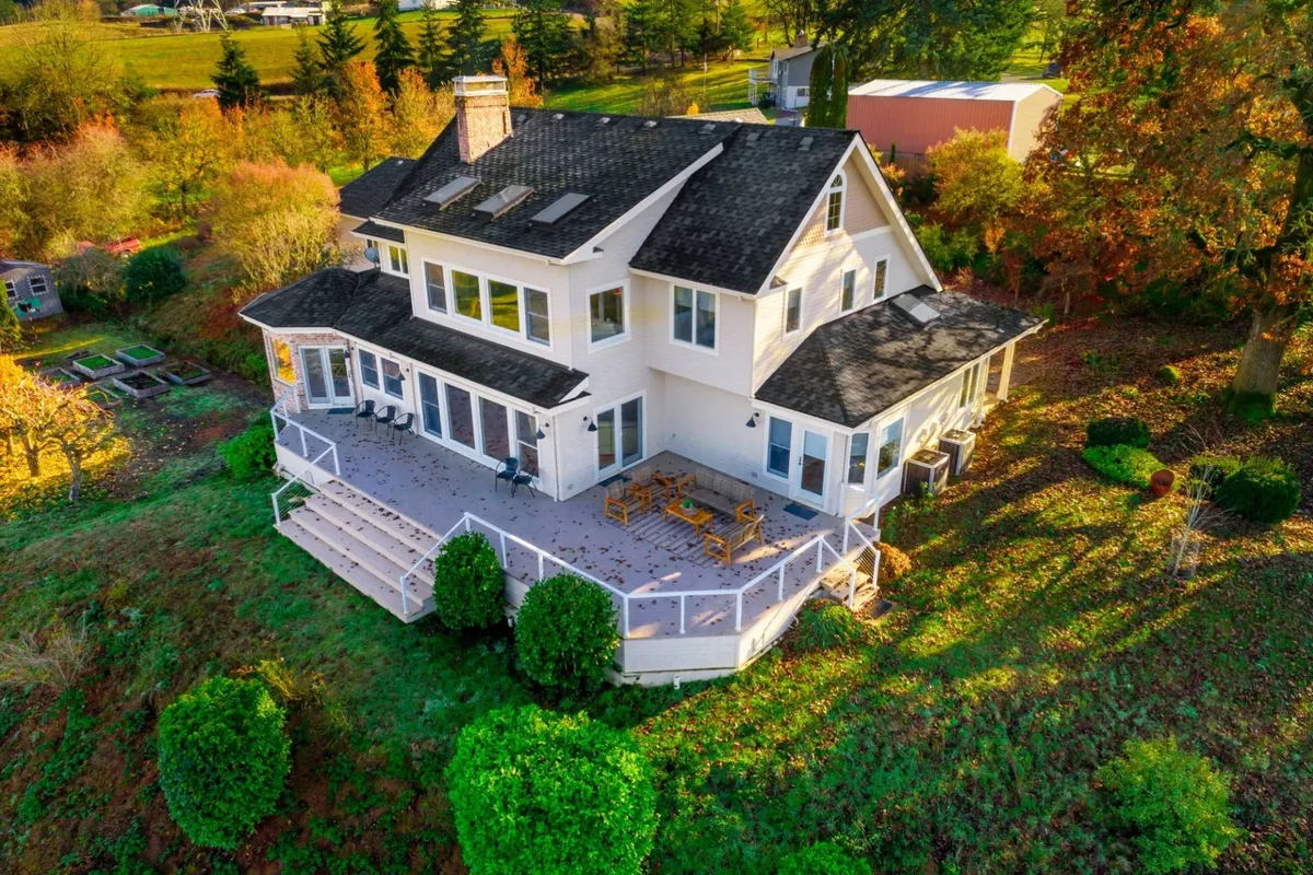 A large wooden deck overlooks a landscaped garden and is surrounded by trees, with expansive windows reflecting the outdoors. The serene setting is ideal for dining or relaxing while soaking in sunset views, embodying luxury living amidst nature.