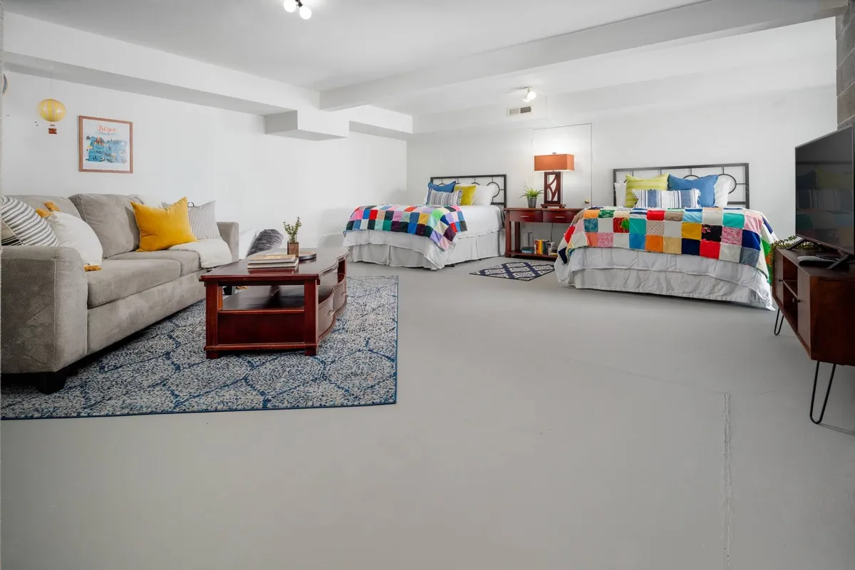 A comfortable area with two colorful beds, a plush sofa with decorative pillows, a coffee table, and a large TV. The casual layout invites relaxation, movie nights, and socializing.