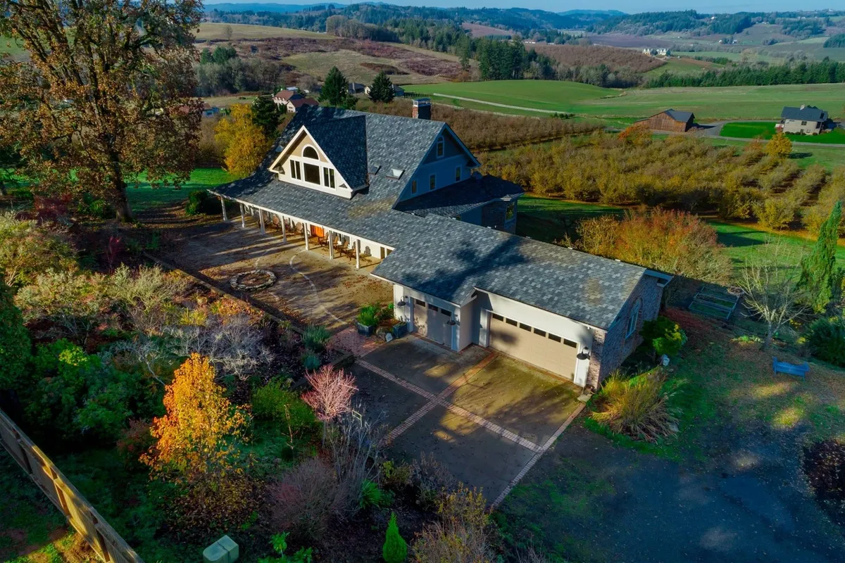 The image showcases the elegant exterior of Skyview Villa set against rolling hills and lush, landscaped gardens. The driveway leads up to the spacious house, and the sweeping valley and vineyard views create a tranquil, picturesque setting. The porch and outdoor spaces hint at perfect spots for gatherings or relaxing while watching the sunset.