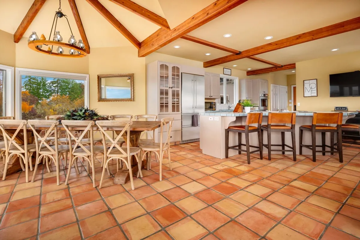 This image displays a generous dining table paired with a nearby kitchen island and large windows, emphasizing an open, sociable layout ideal for group gatherings and shared meals. The setting is warm and filled with natural light, enhancing the atmosphere of celebration.