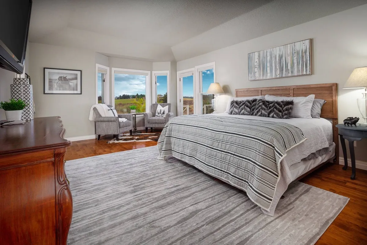 This image features a king-size bed with decorative pillows set against a serene backdrop. Large windows showcase sweeping scenic views, and a comfortable seating area is tucked beside the window. The overall mood is cozy and tranquil, making it ideal for restful moments and waking up to natural beauty.