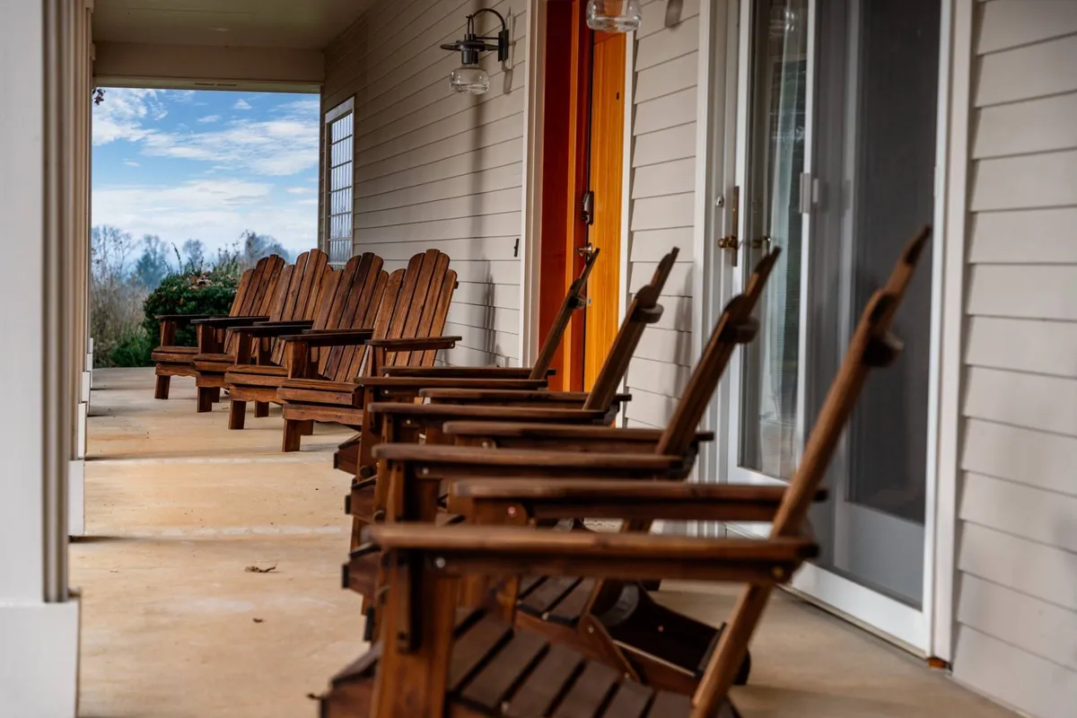 This image displays the front entrance of Skyview Villa, featuring two wooden rocking chairs placed on a covered porch. The entrance door and outdoor light fixtures are visible, with the peaceful surroundings inviting guests to sit and take in the view.