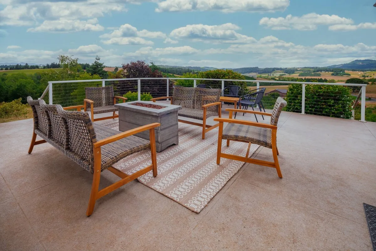 An inviting outdoor space with a fire pit surrounded by comfortable seating, overlooking open fields and rolling hills. The landscape offers unobstructed views of the countryside, perfect for relaxing or socializing at sunset or under the stars.