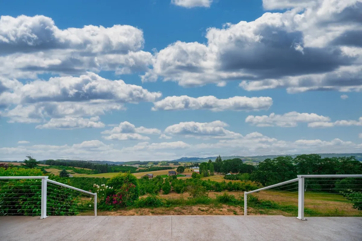 A panoramic view of vast rolling hills and open fields stretching into the distance, under a dramatic sky. The scenery invites guests to embark on nature walks, explore the land, or simply enjoy the peaceful surroundings.