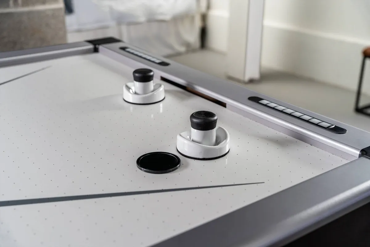 A close-up of an air hockey table, complete with pucks and goal openings, set up for action. The lighting and composition highlight the table as a hub for energetic, competitive fun.